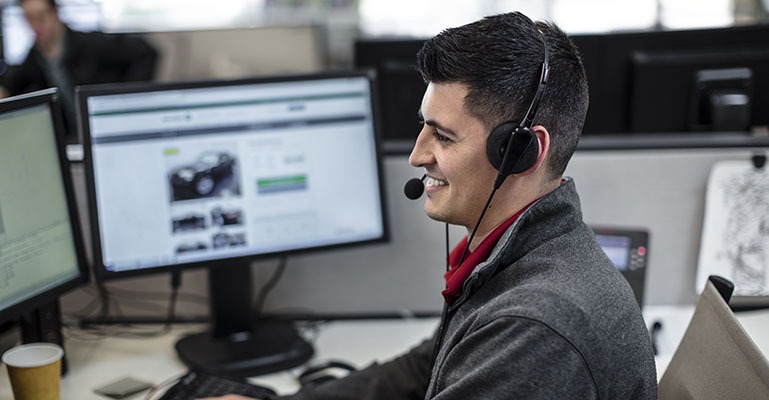 A help desk employee wearing a headset smiles while talking to a customer.