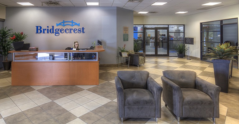 A receptionist sits behind a desk in a large, welcoming foyer area with the Bridgecrest logo on the wall.